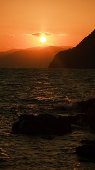 Breathtaking ocean view of the sunset with silhouetted rocky cliffs and warm hues.
