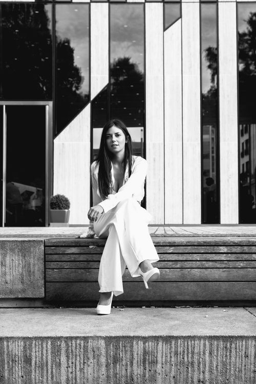 Free Black and white portrait of a stylish woman in white attire sitting outdoors in Düsseldorf. Stock Photo
