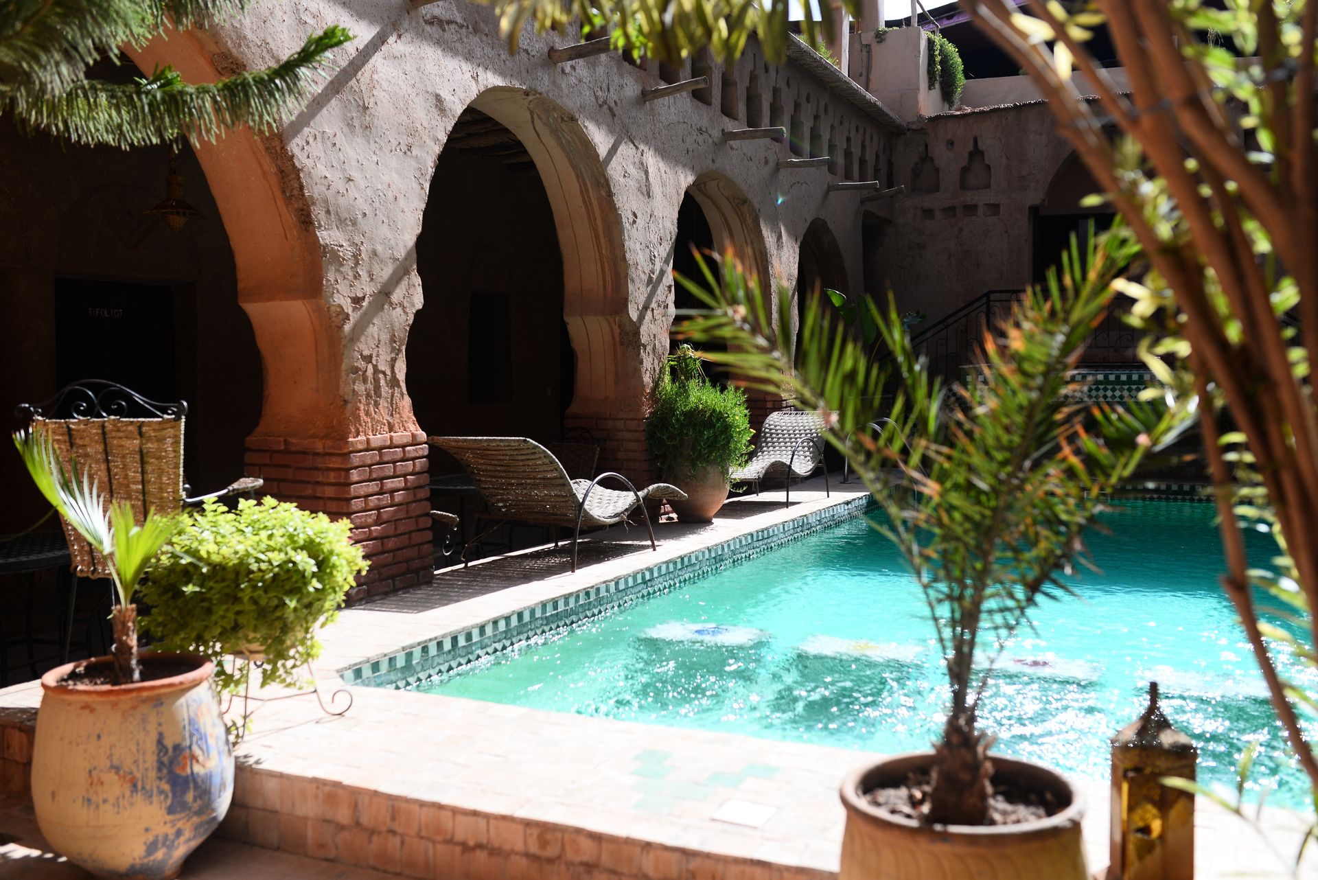 A tranquil luxury courtyard featuring a beautiful swimming pool and elegant architecture under a sunny sky.