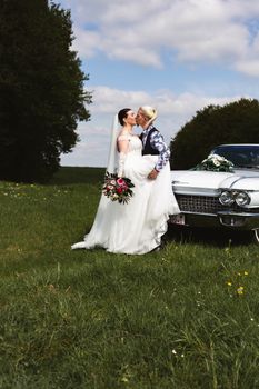 Bride and groom sharing a kiss in a scenic outdoor setting with a classic car.