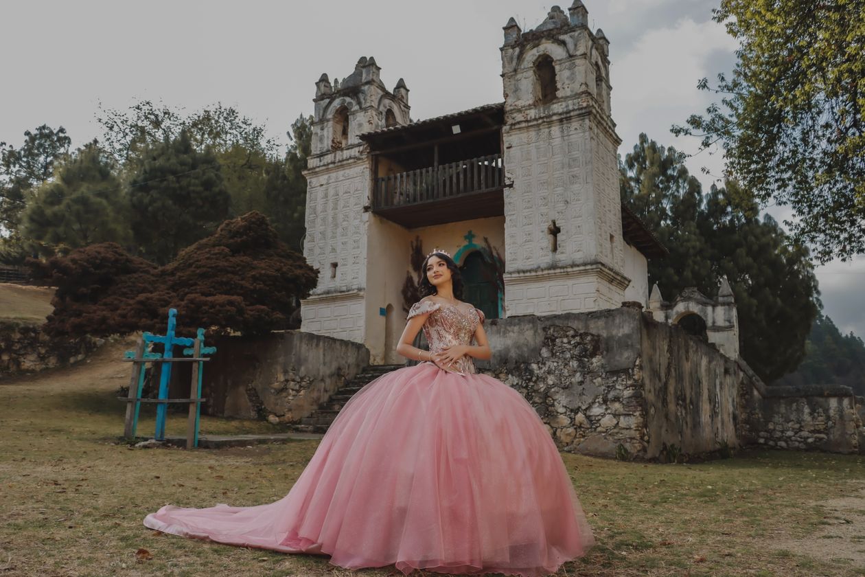 Young woman in a pink ball gown with a long train in front of an old church