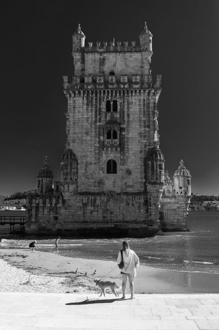 Black and white photo of Belem Tower in Lisbon, featuring a visitor with a dog on a sunny day.