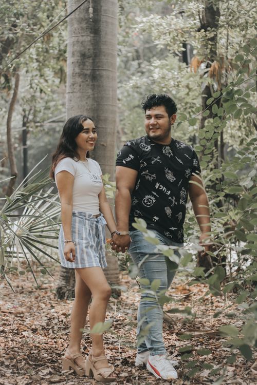 Free A happy couple holding hands while walking through a lush, green forest during the day. Stock Photo