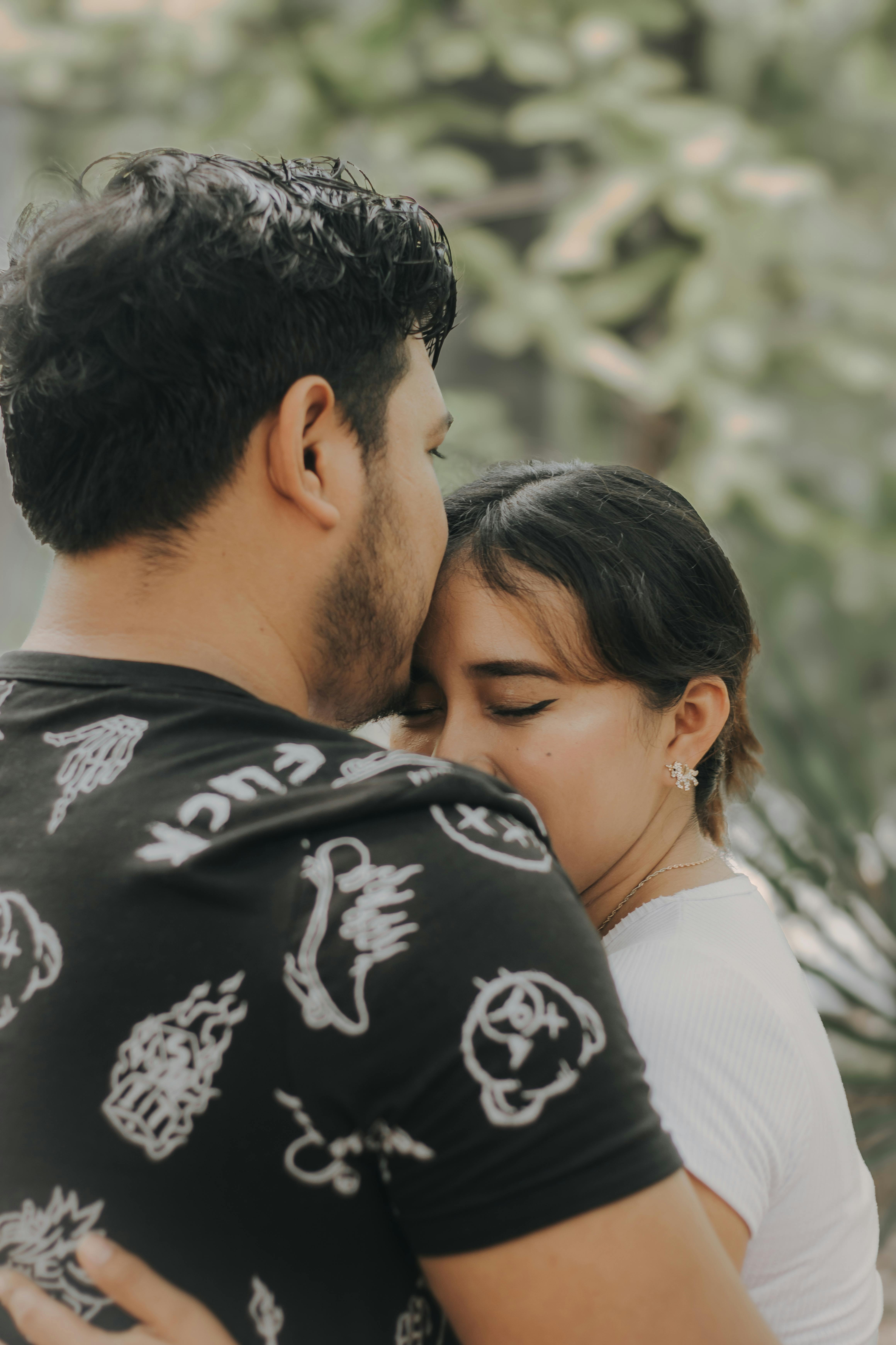 a man and woman hugging each other in front of a tree