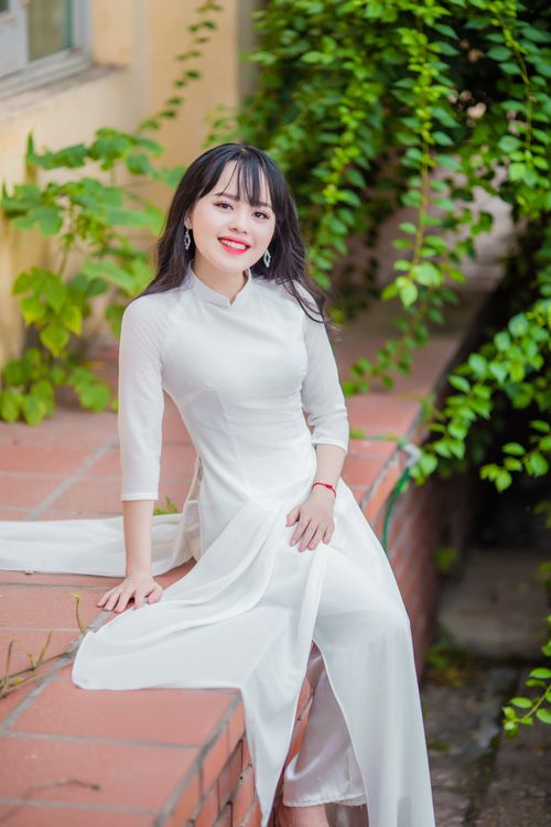 Free A young woman in an elegant white dress sits outdoors, exuding grace and style. Stock Photo