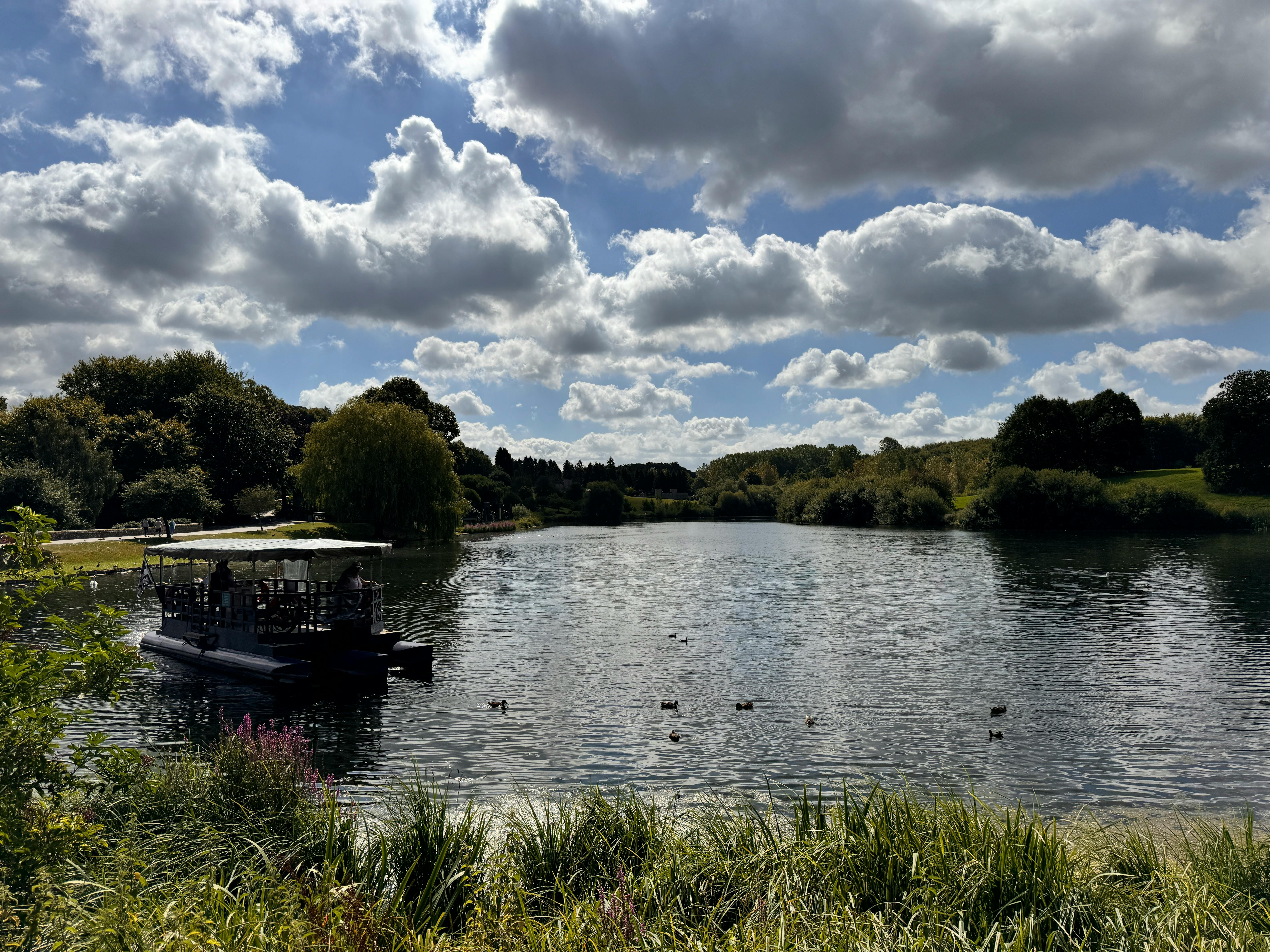 A serene summer day at Leeds Castle's lake with a boat and lush greenery.