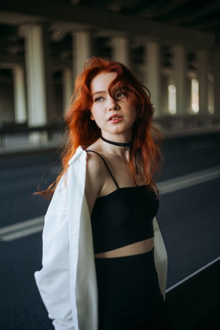 Stylish ginger-haired woman in a chic outfit poses confidently outdoors creating an urban vibe.