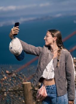 Woman takes selfie at scenic overlook with view of the bay and bridge.