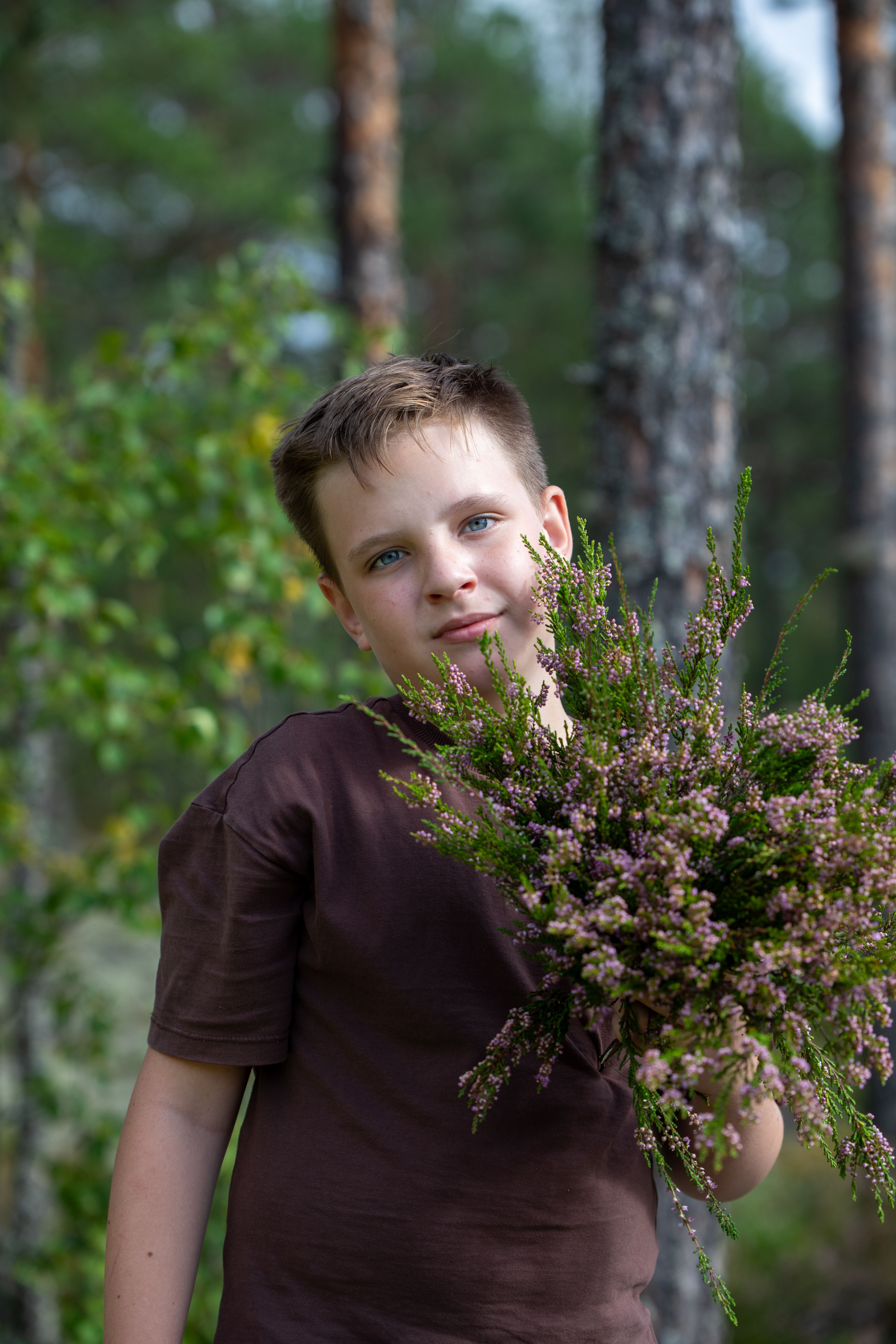 Young boy smiling while holding a bouquet of wildflowers in a lush forest.