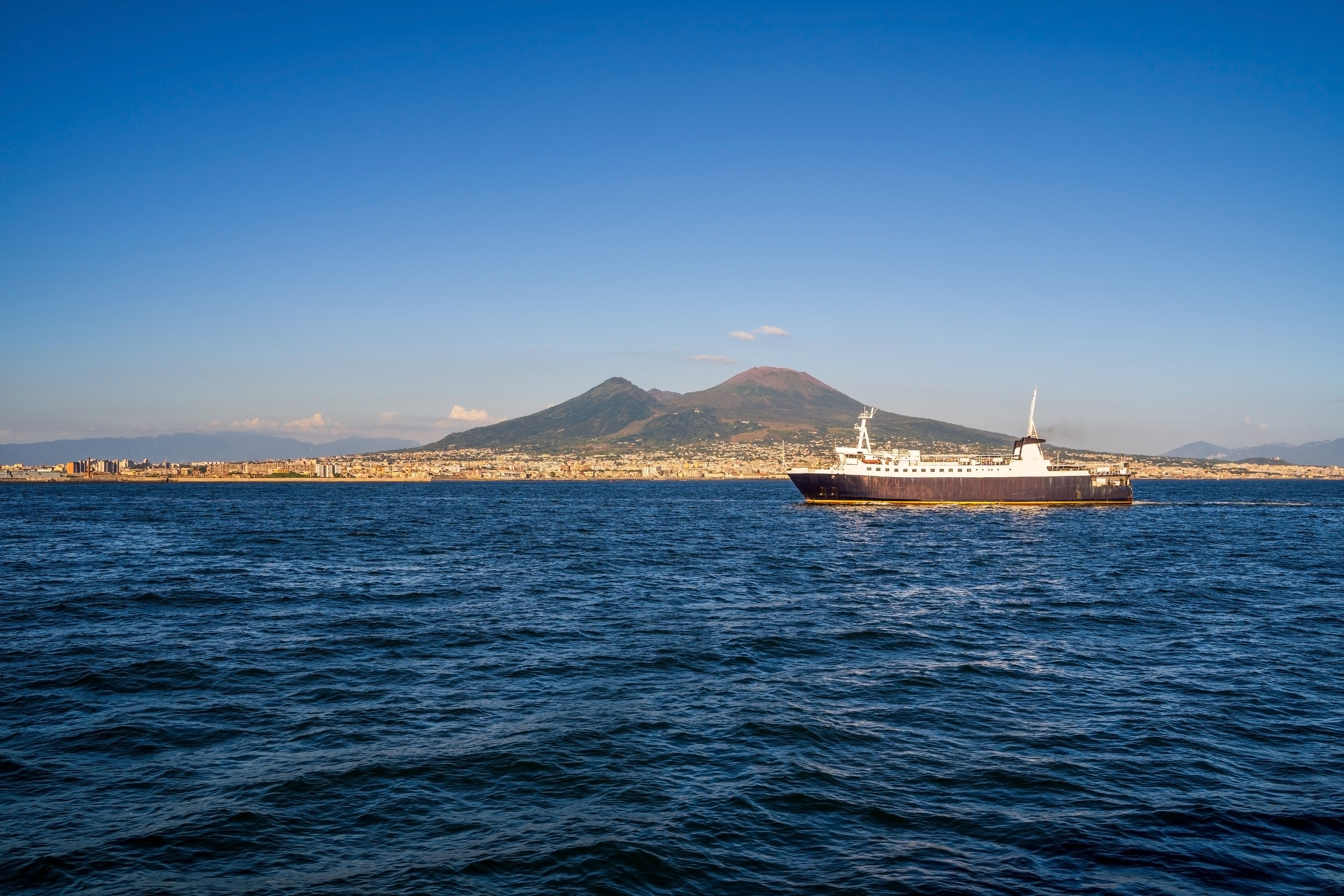 Ferry crossing the sea with Mount Vesuvius in the background under a clear summer sky.
