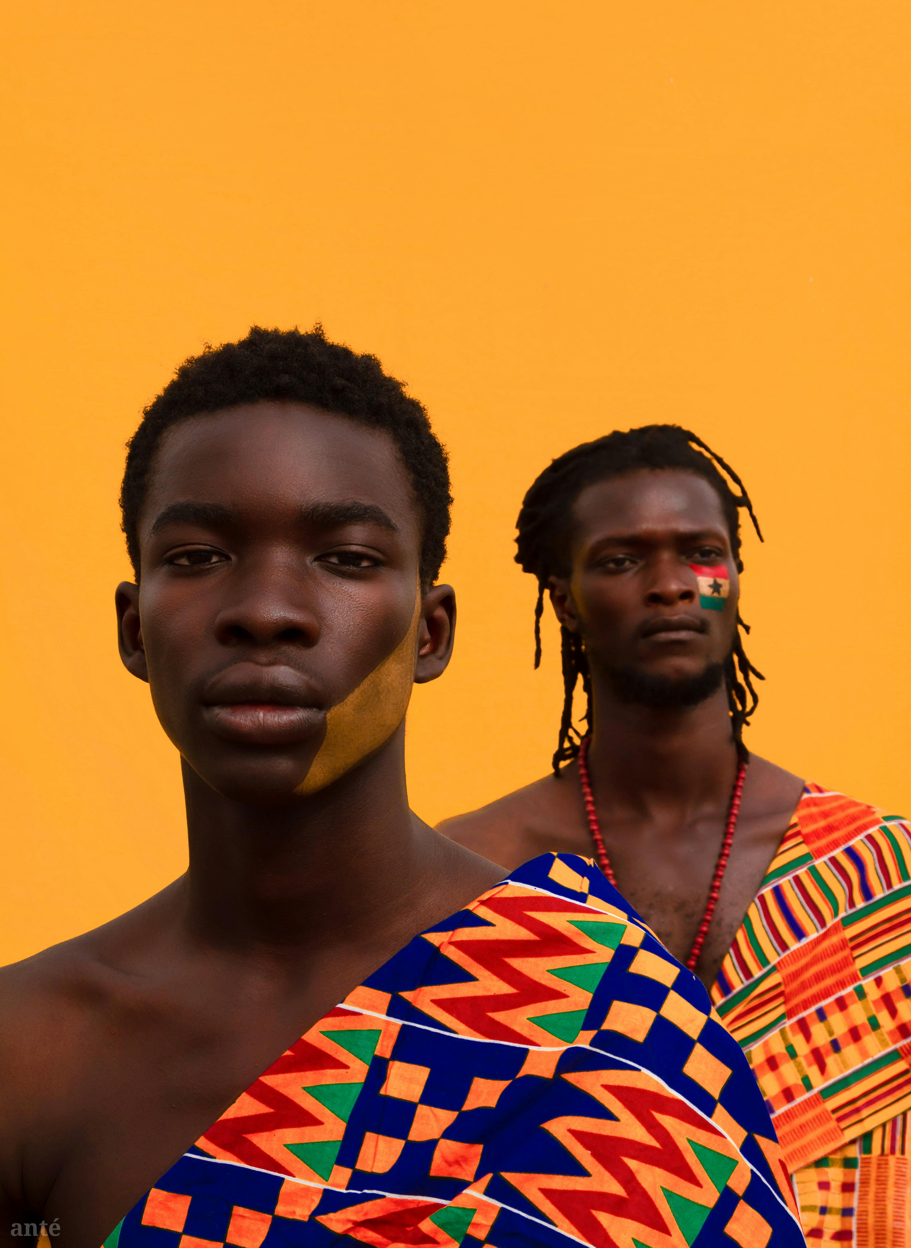 Two men in traditional vibrant attire with face paint, expressing cultural pride.