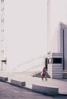 A lone woman walks past contemporary architecture in sunny Madrid, Spain.