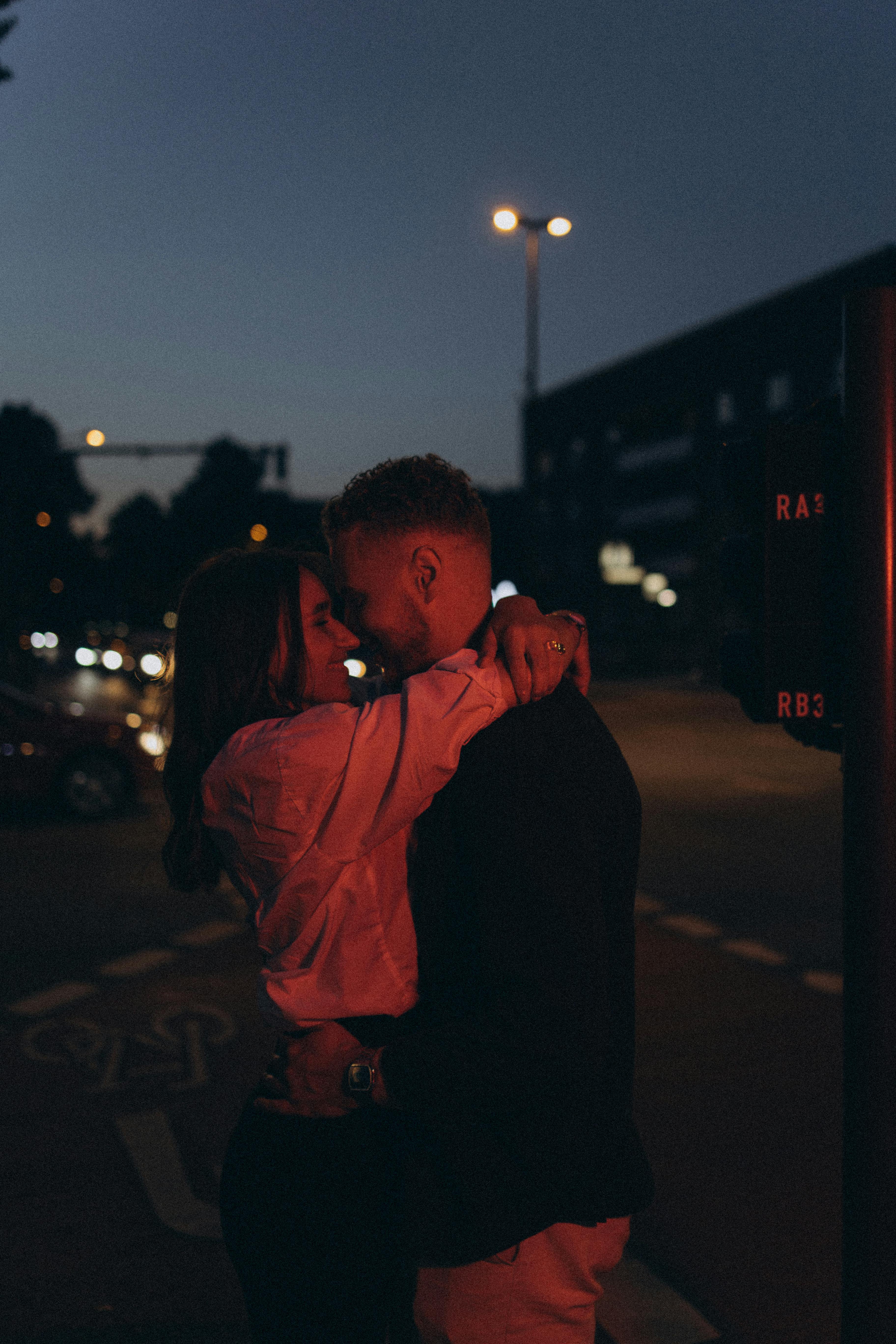 A couple shares a tender embrace on a city street during twilight, capturing a moment of romance.