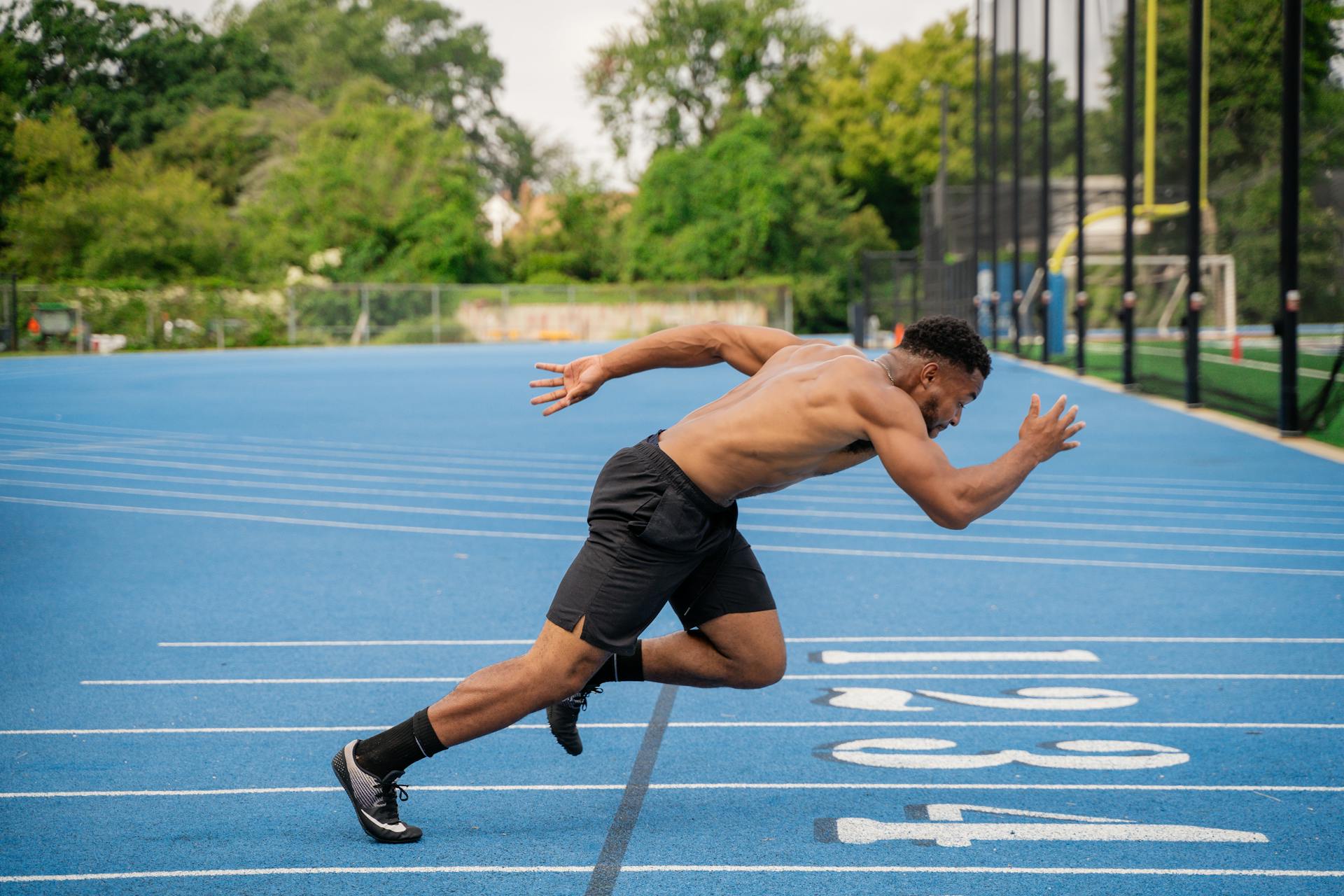 A male athlete intensely sprints on a vibrant blue outdoor running track. Perfect for sports and fitness themes.