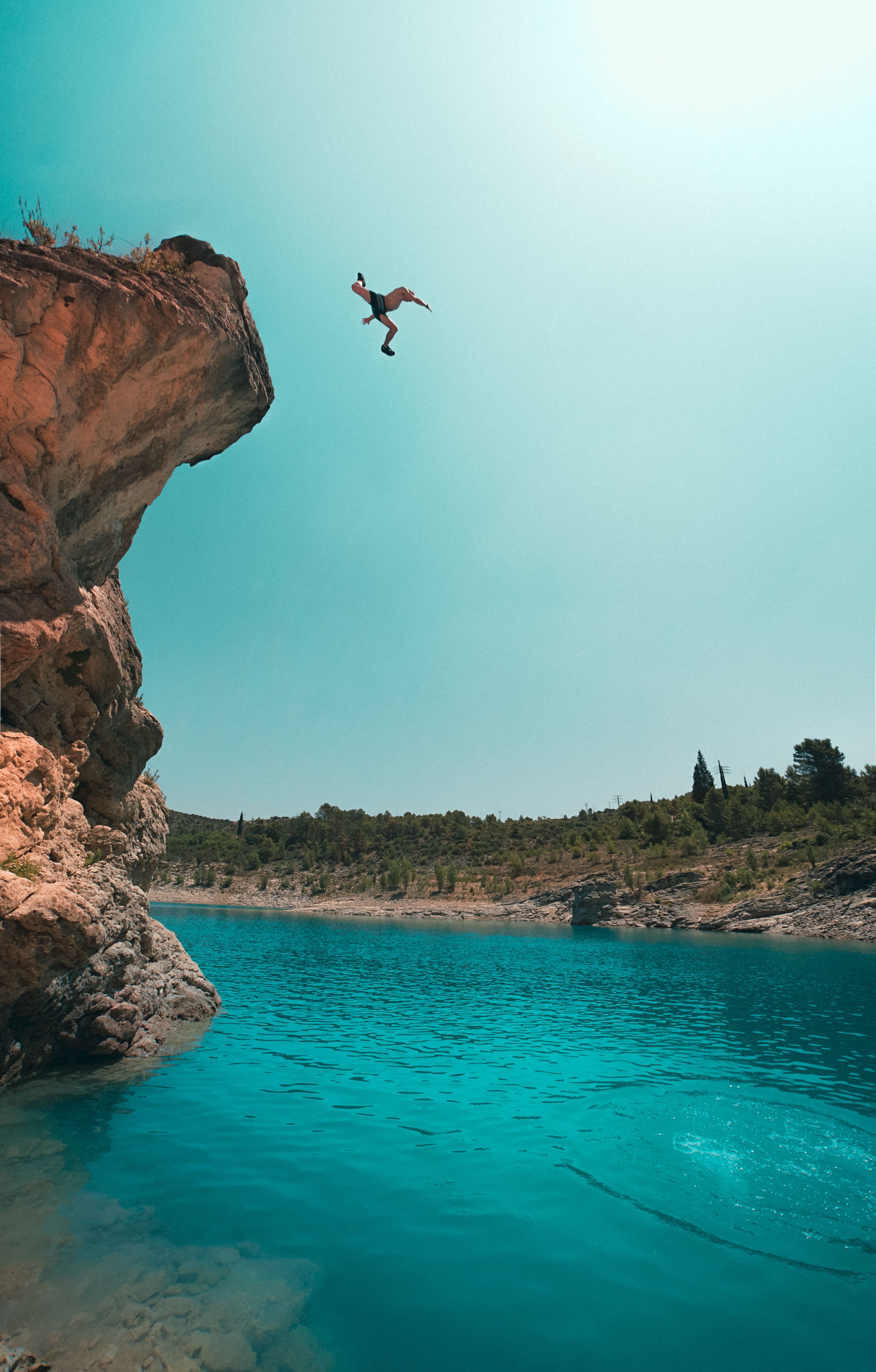 A person jumping off a cliff into a lake · Free Stock Photo