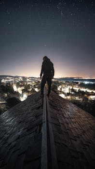 Silhouette of person on rooftop against starry night over illuminated cityscape.