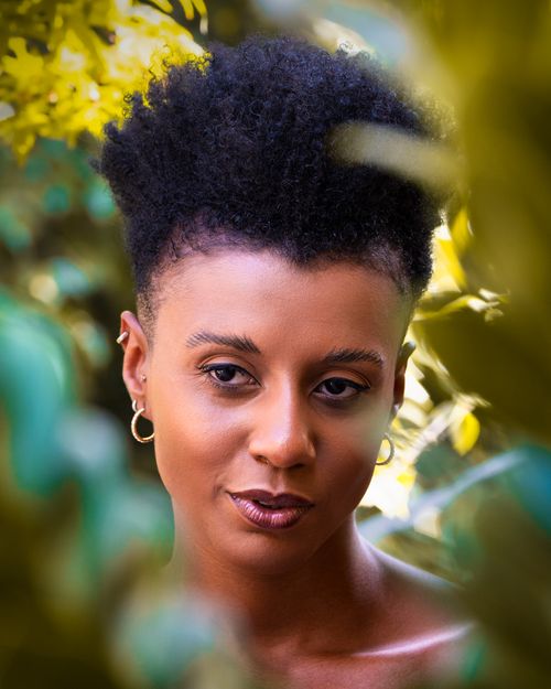 Free Stunning portrait of a woman with an afro, captured outdoors amidst vibrant greenery. Stock Photo