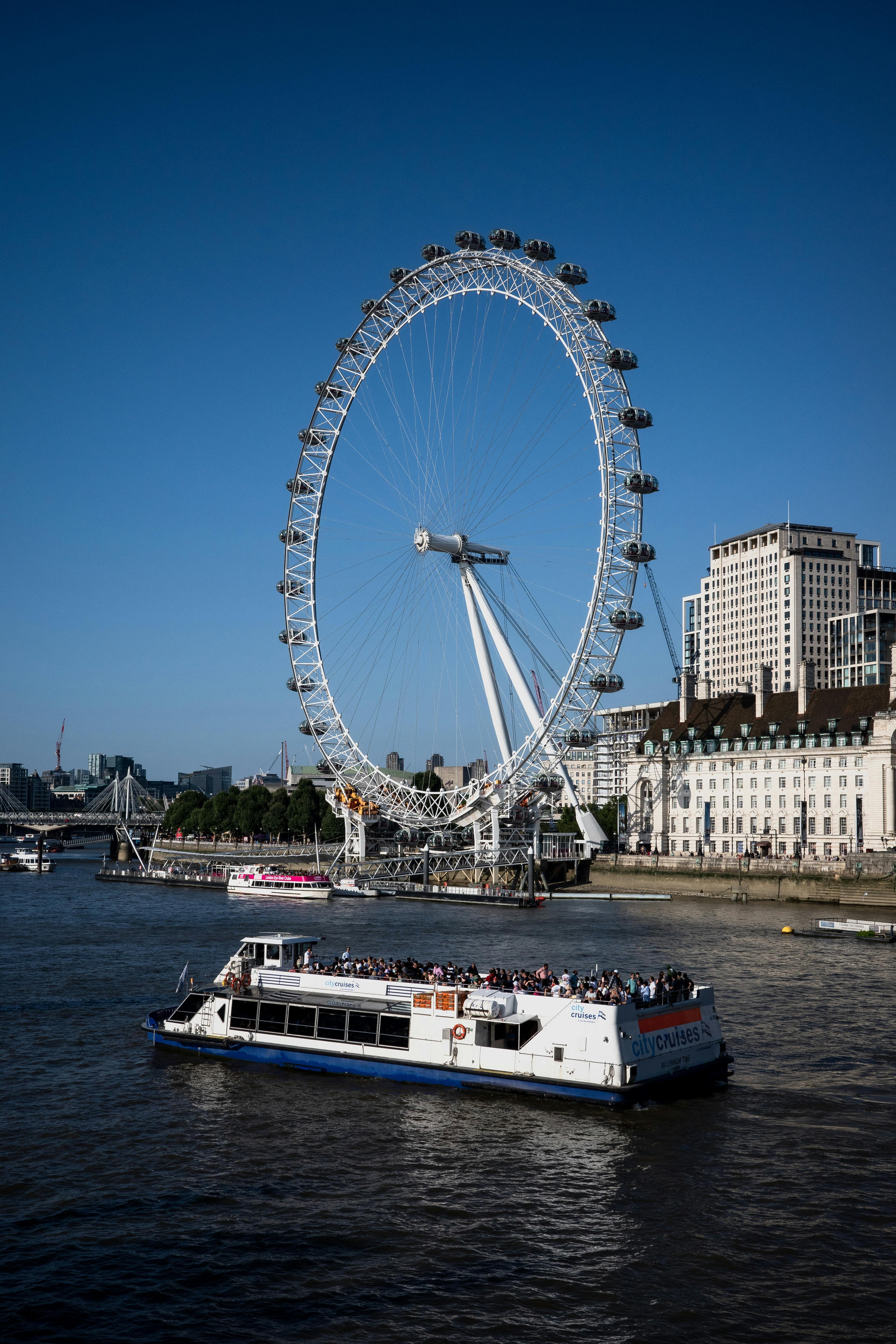 View of London Eye with boat on Thames River, sunny day.