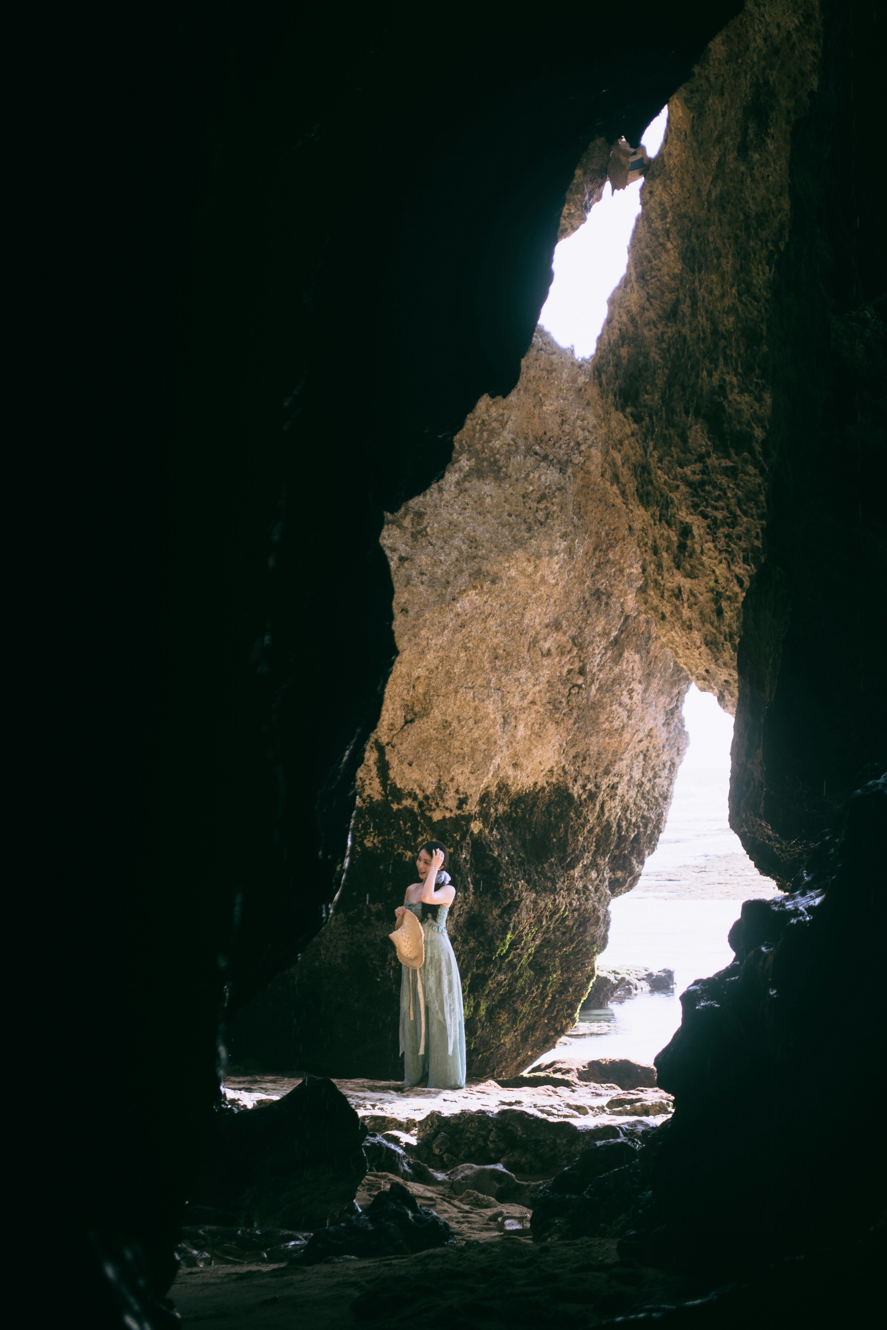 A woman stands in a sunlit coastal cave, capturing the beauty of nature and exploration.
