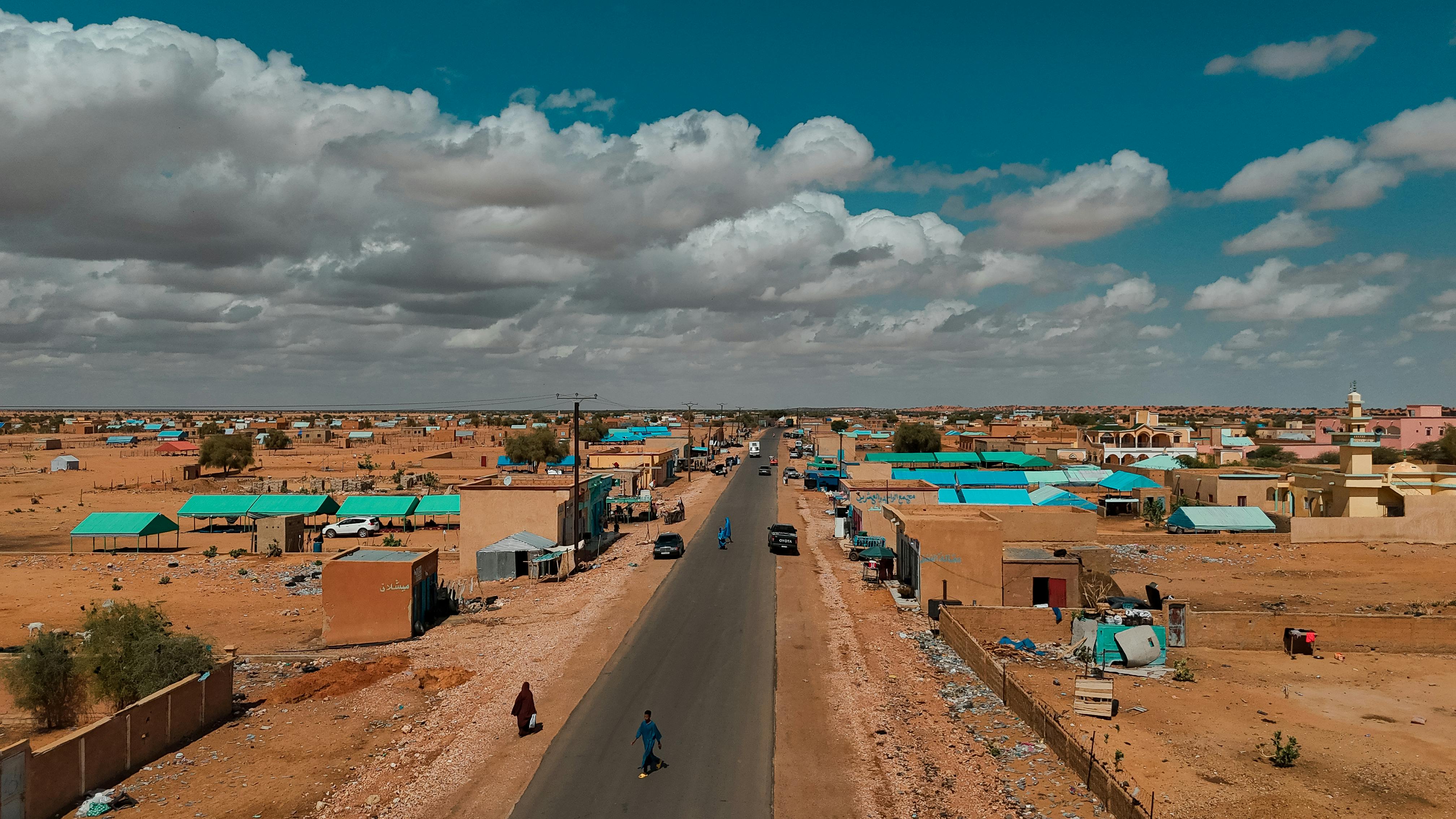 Aerial shot of a town in the desert with houses and a main road under a cloudy sky.