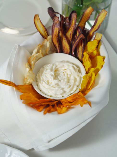 A bowl of creamy French onion dip flecked with deep golden caramelized onions, surrounded by ridged potato chips on a wooden board.
