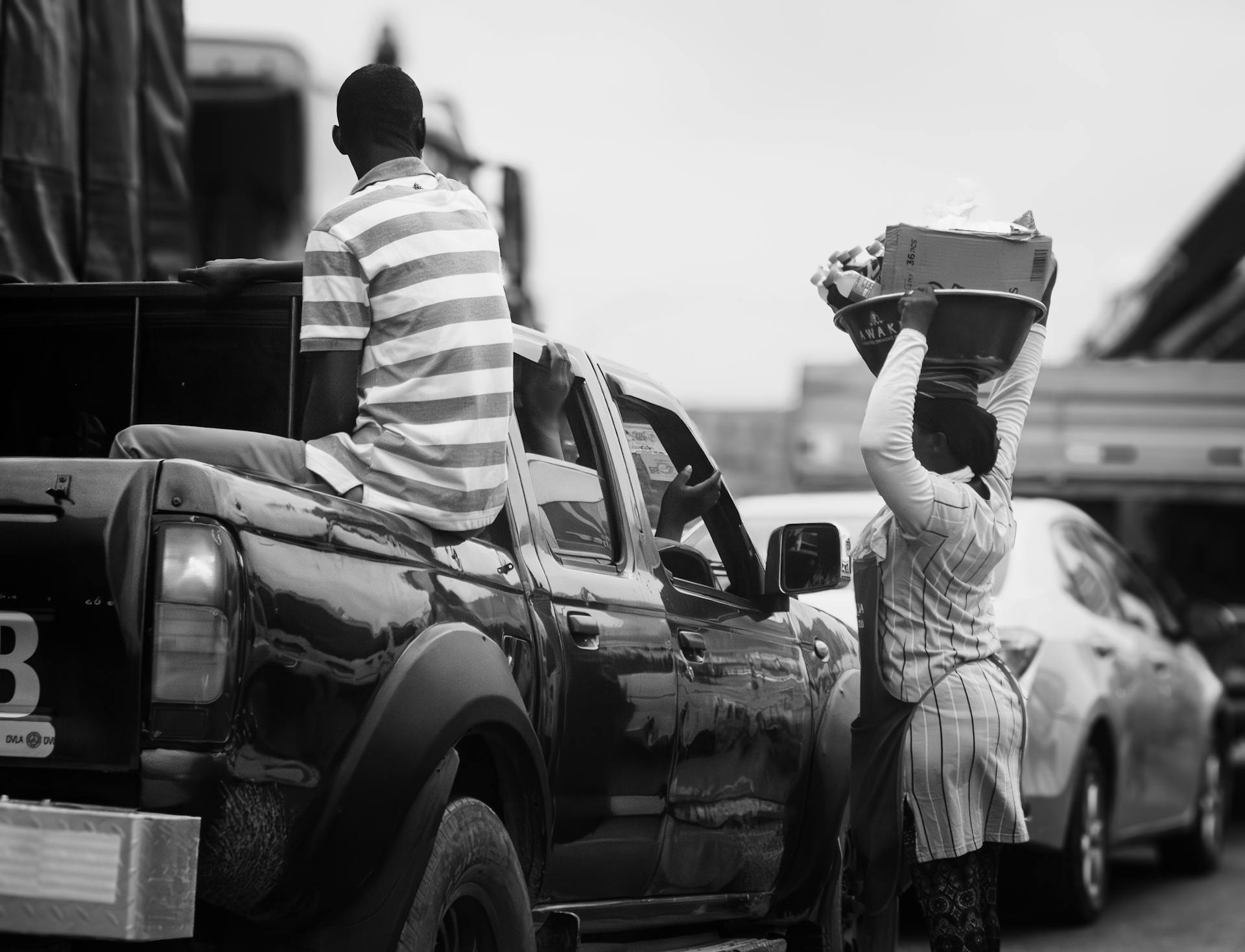 A street vendor balances goods on her head amidst traffic in Accra, Ghana. Capturing urban life.