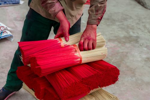Free A worker handling bundles of traditional red incense sticks in an outdoor setting. Stock Photo
