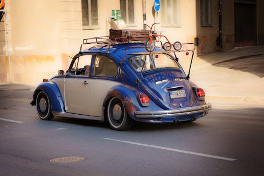 Vintage blue Volkswagen Beetle with luggage, traveling on a sunny street.