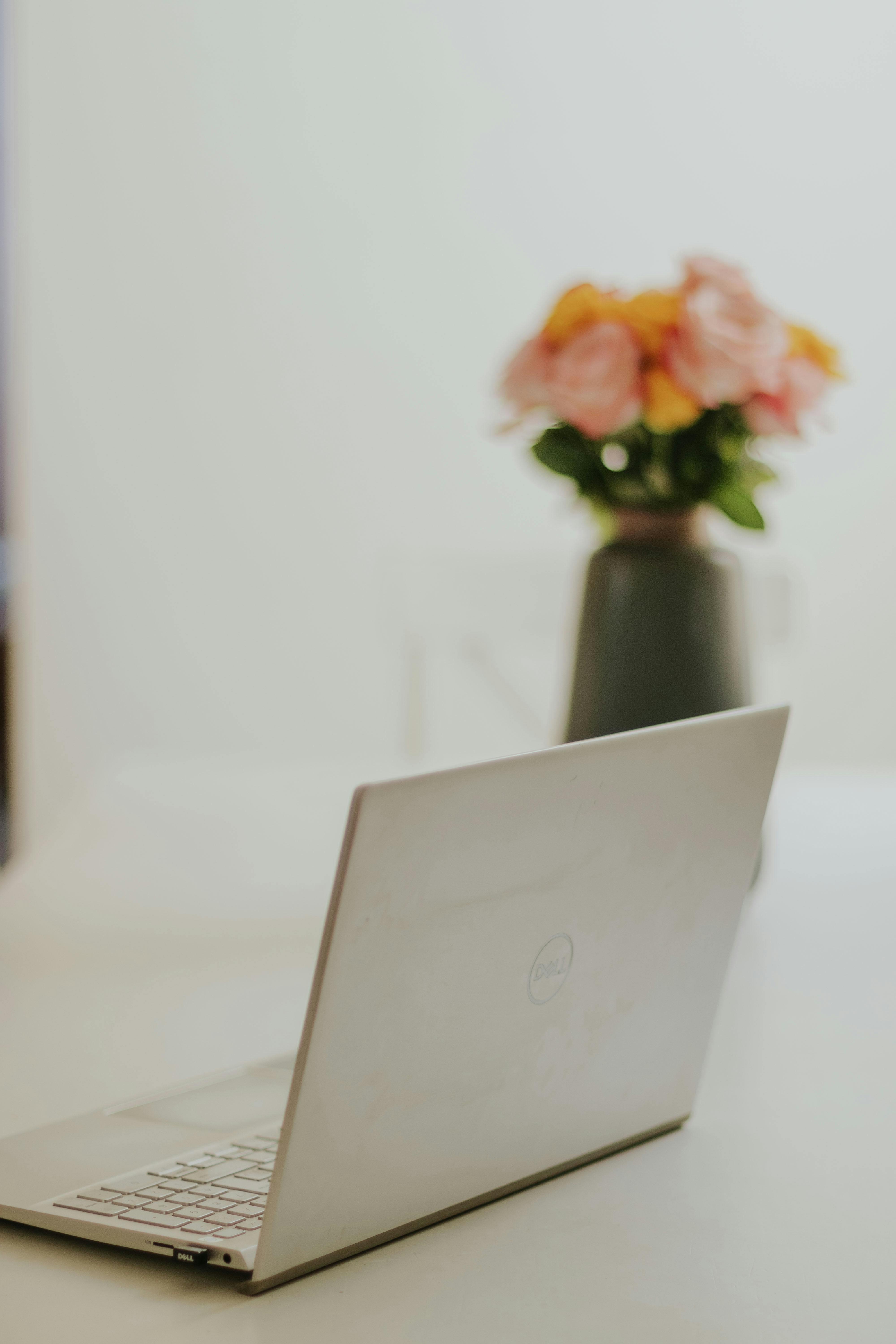 A minimalist home office setup featuring a sleek laptop and a vase of colorful flowers on a desk.