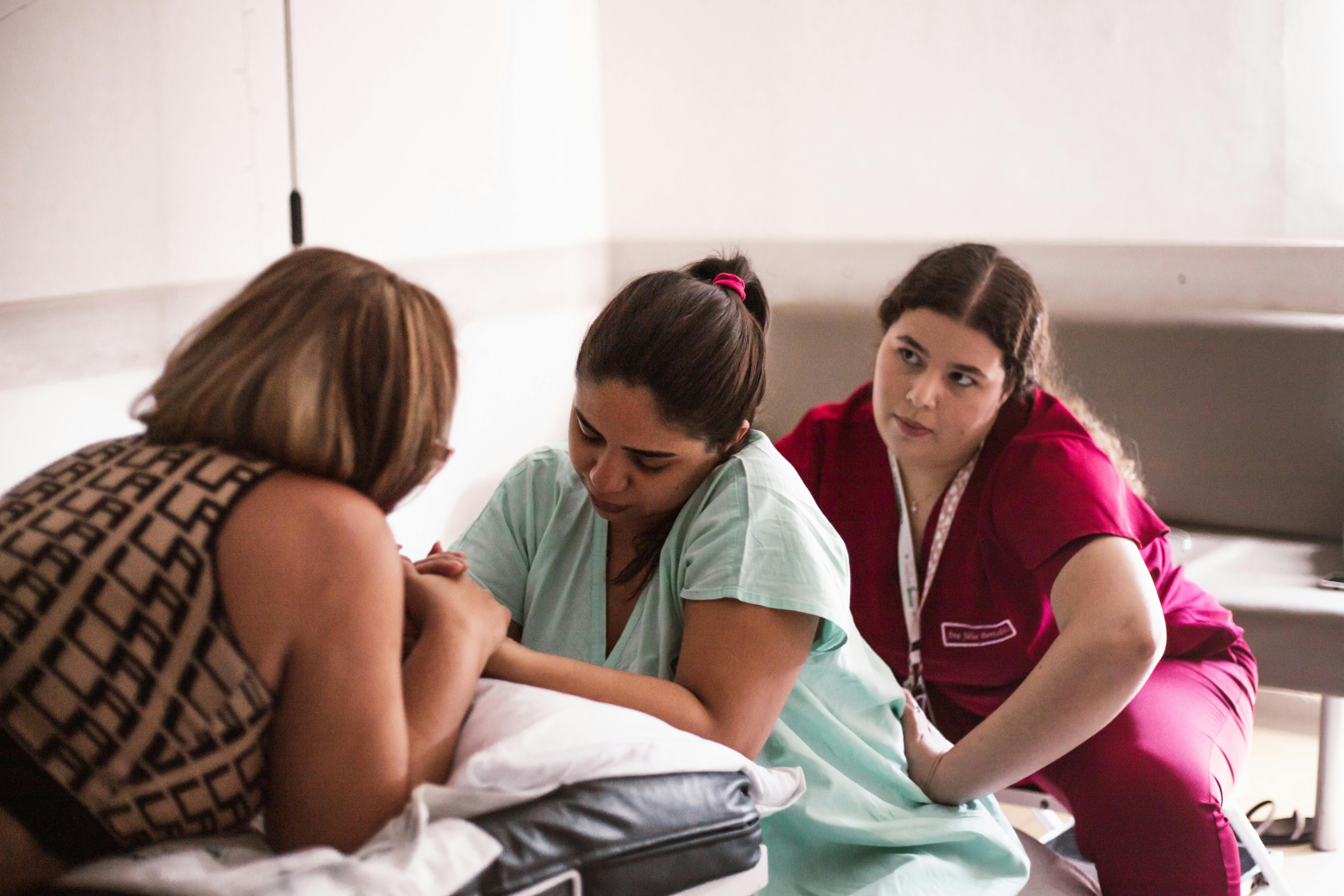 two women in scrubs are talking to a woman in a hospital bed