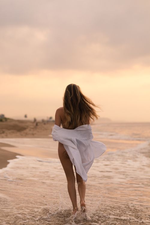 A woman walking in the ocean at sunset · Free Stock Photo