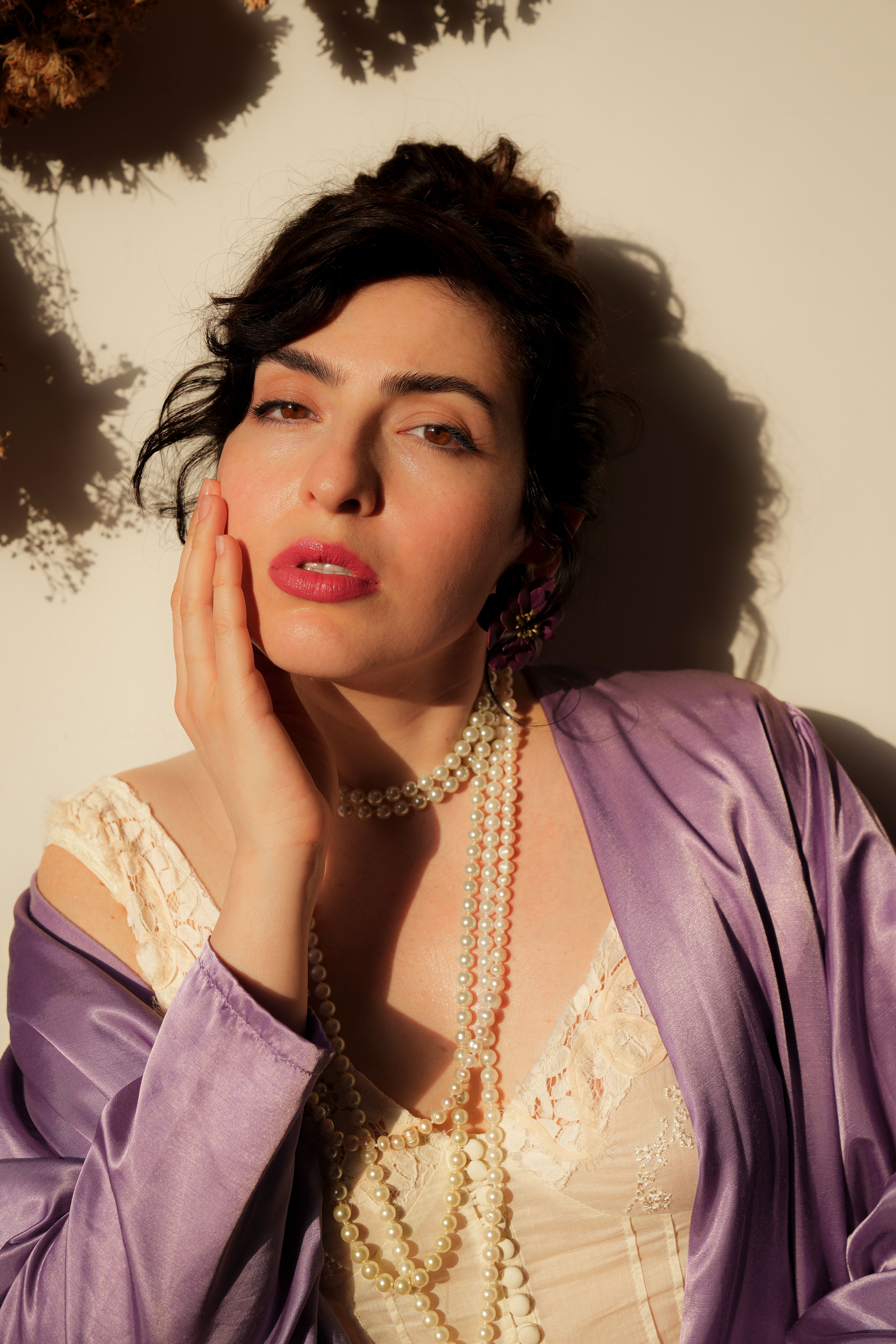 A glamorous woman poses with pearls and satin in warm lighting.