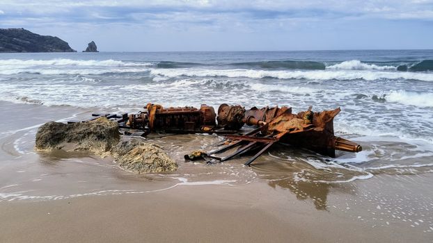 A dramatic view of a rusty shipwreck on a sandy Corfu beach under cloudy skies.