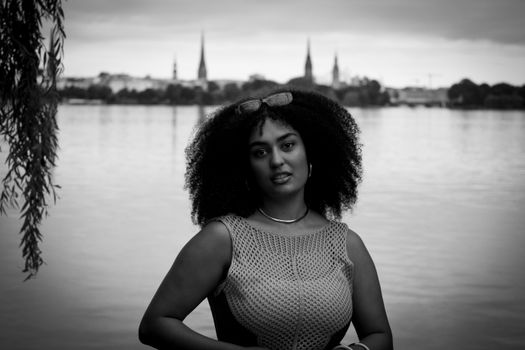 Black and white portrait of a woman by Alster Lake, Hamburg, showcasing city skyline.