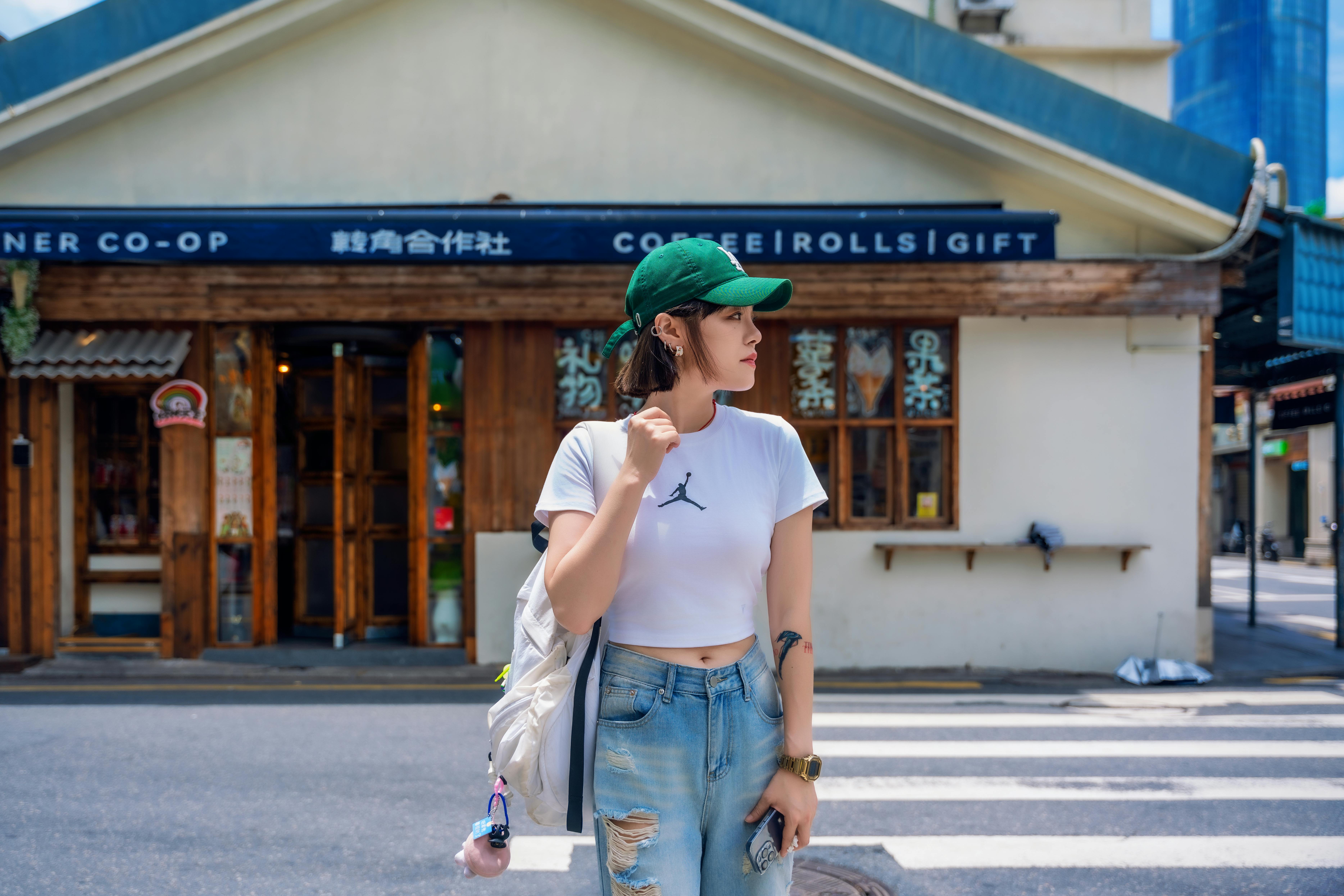 a woman in a green hat and white shirt is standing on the street