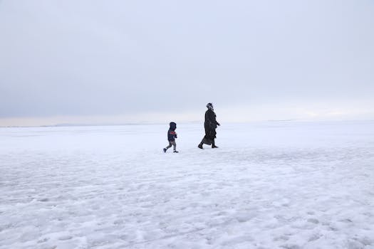 A child and adult walk across a vast snow-covered field in Kars, Turkey. Wintry and serene.