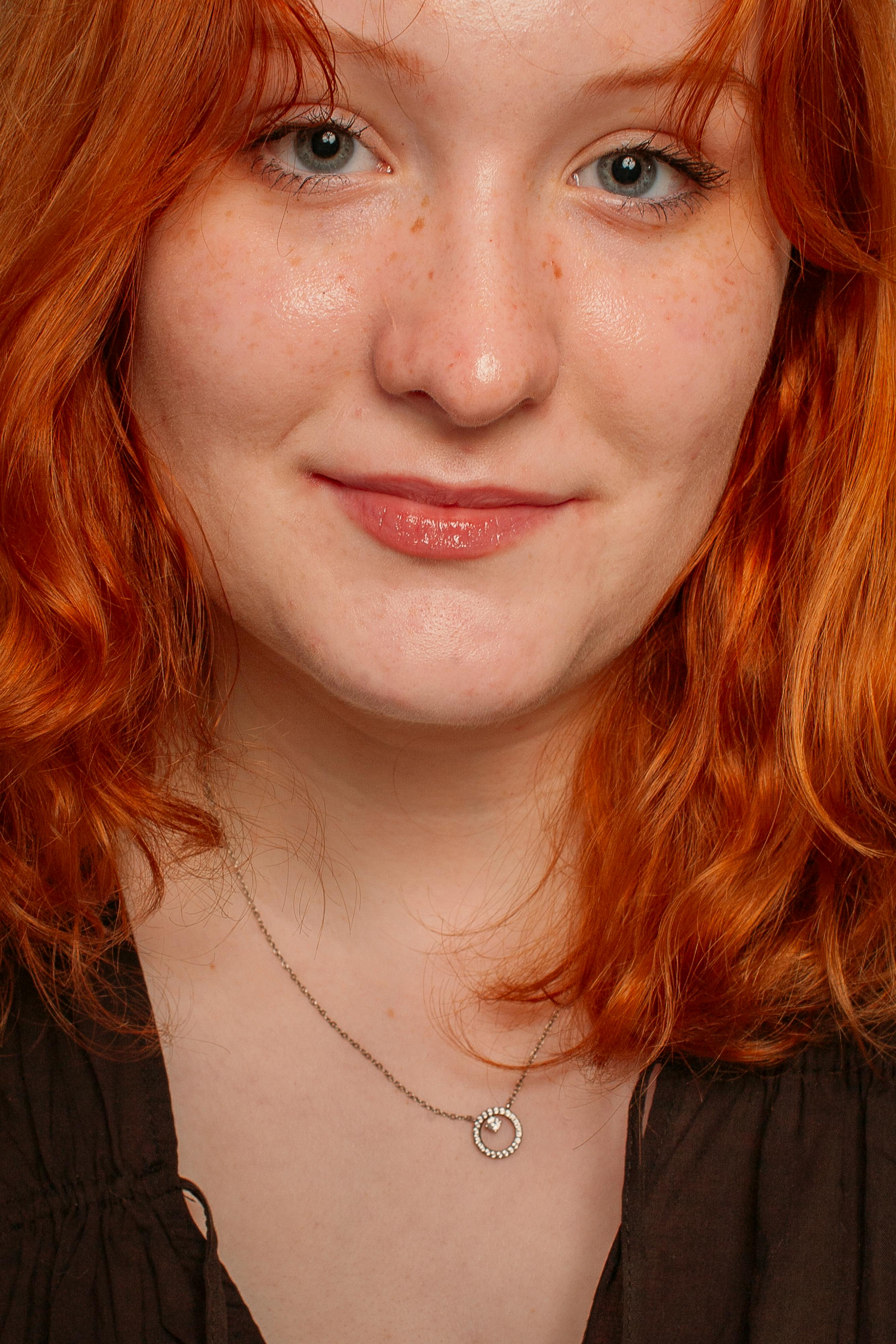 Close-up portrait of a young redhead woman with freckles and light makeup.