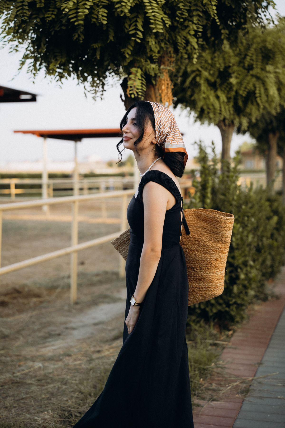 Woman at sunset in elegant summer dress with a straw bag