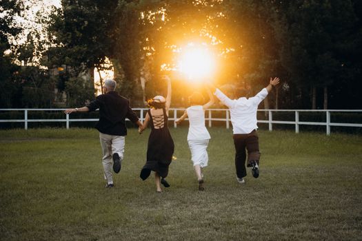 Four adults joyfully running towards the sunset in a green field, capturing a lively and carefree moment.