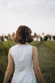 Back view of a woman in a white dress walking in a field at sunset, embodying tranquility and style.