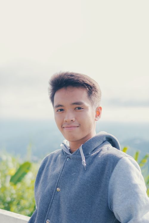 Free A young man in a casual hoodie smiles warmly in a bright outdoor setting. Stock Photo