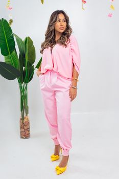 Elegant woman in pink outfit posing indoors with plants, showcasing spring fashion.