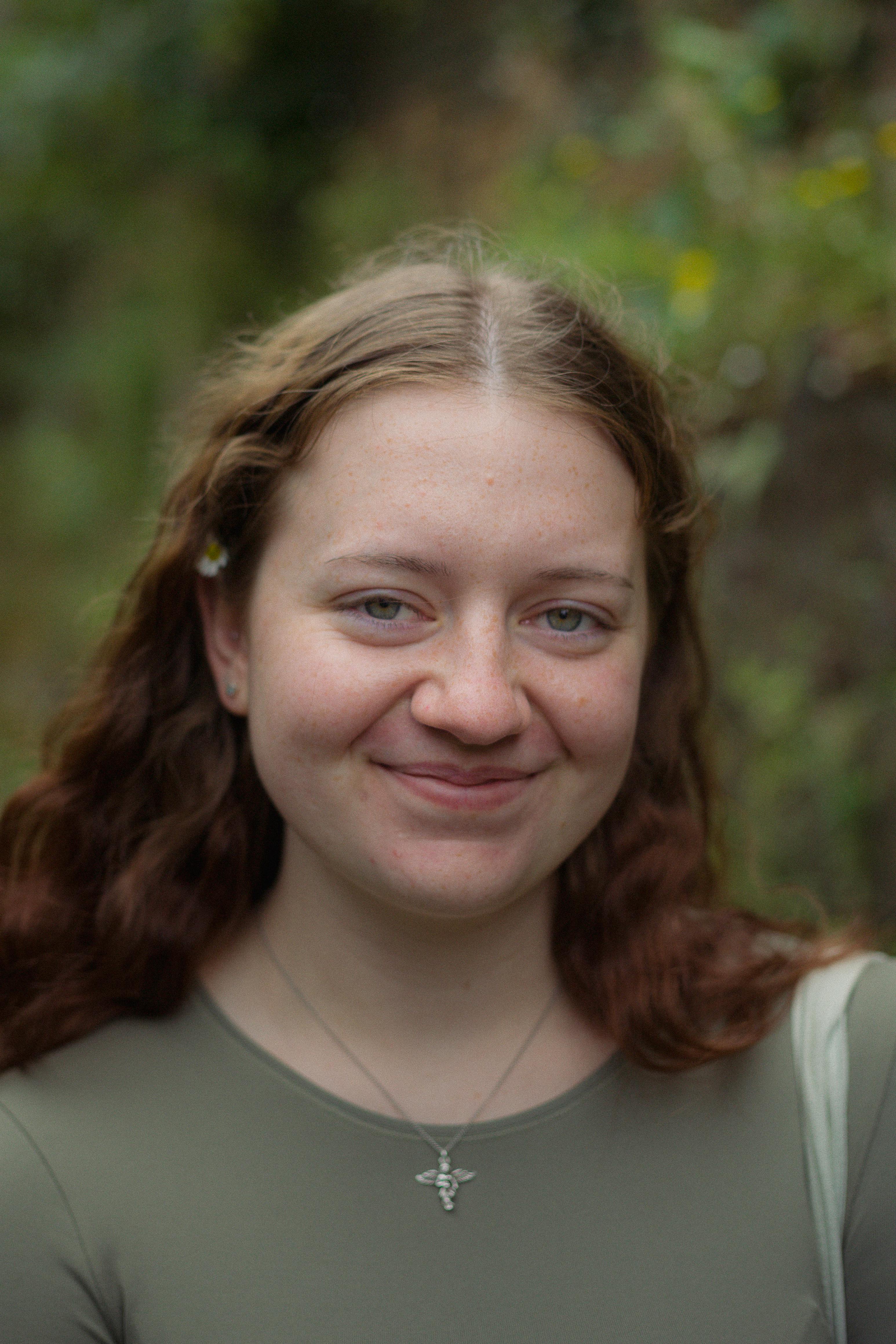 A young woman smiling warmly against a blurred natural background, outdoors portrait.