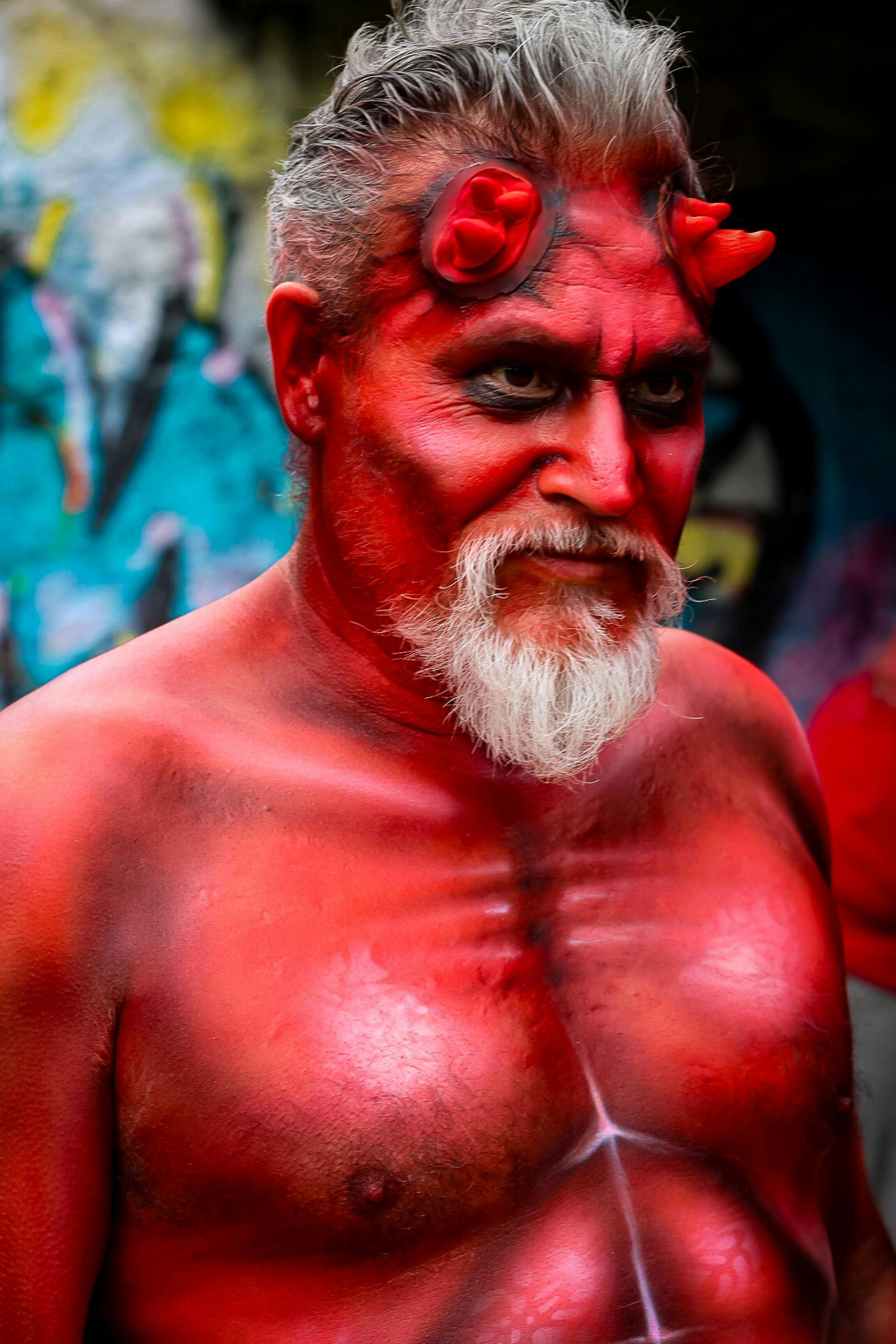 A man with a demonic costume featuring horns and body paint poses outdoors.