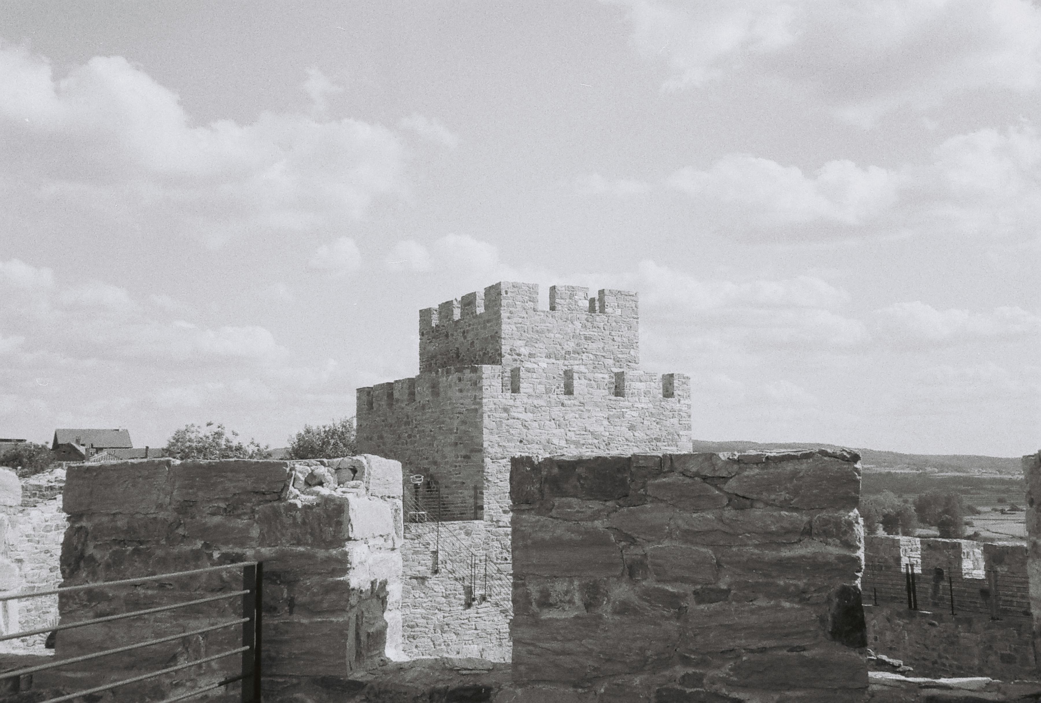 A scenic black and white image of medieval castle walls against a cloud-dotted sky.