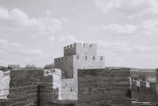 A scenic black and white image of medieval castle walls against a cloud-dotted sky.