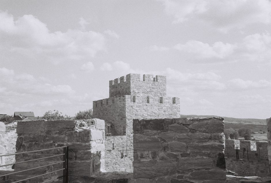 A scenic black and white image of medieval castle walls against a cloud-dotted sky.
