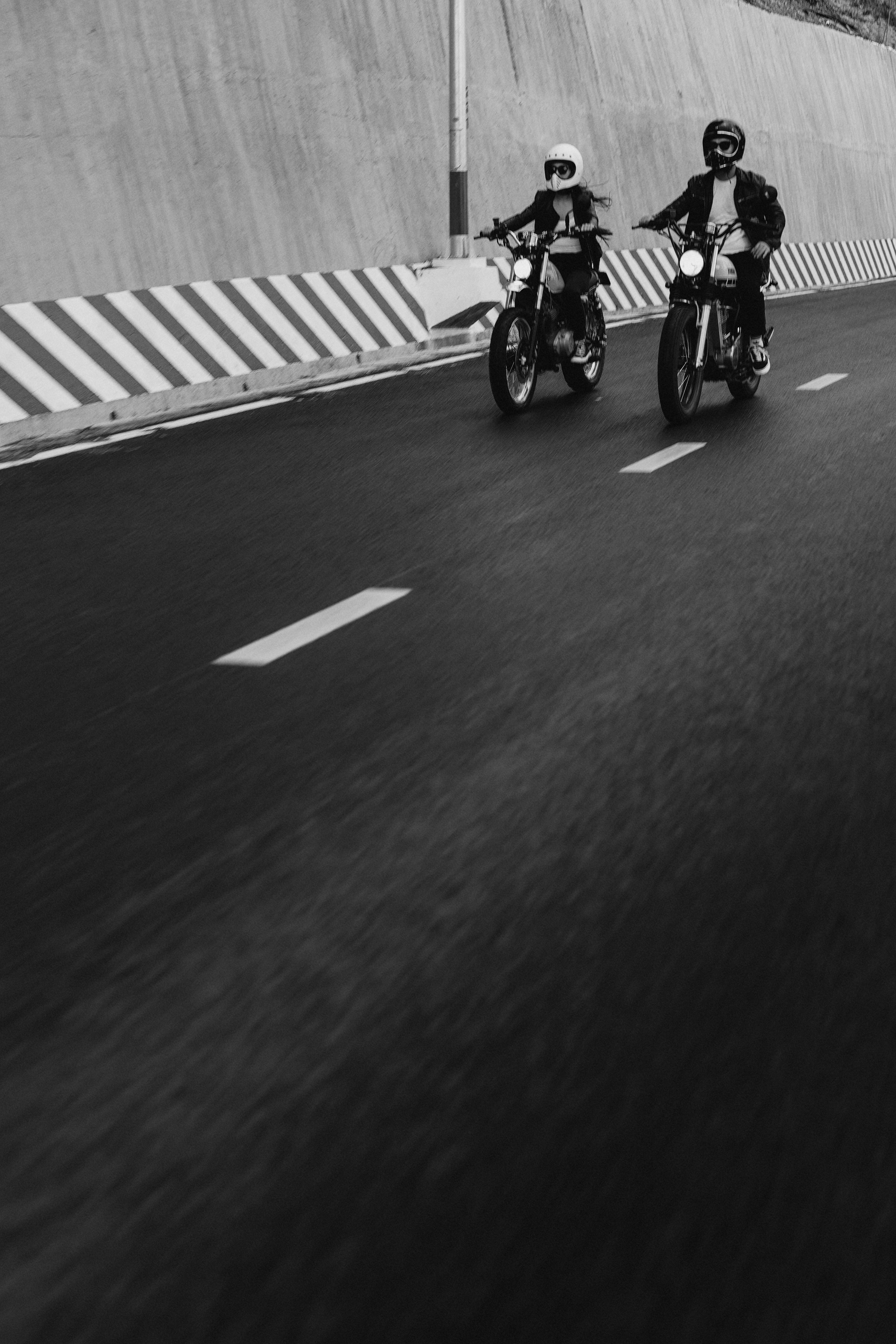 Two motorcyclists riding on an open road in monochrome.