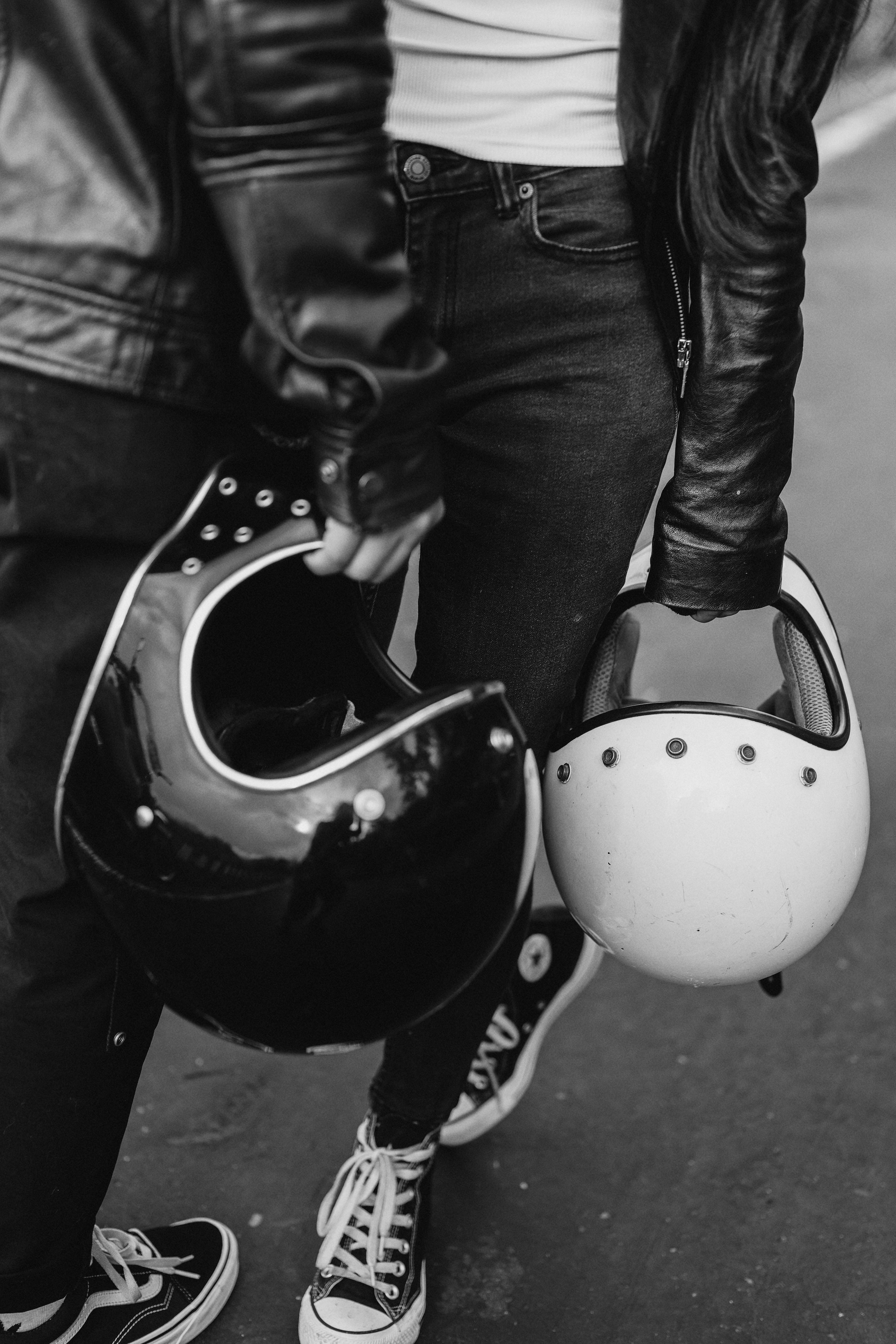 Black and white shot of a fashionable biker couple holding helmets, showcasing urban style.