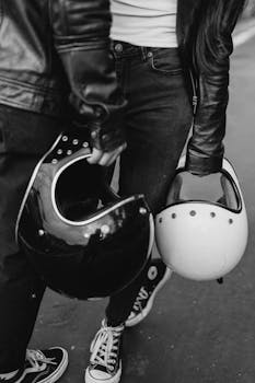 Black and white shot of a fashionable biker couple holding helmets, showcasing urban style.